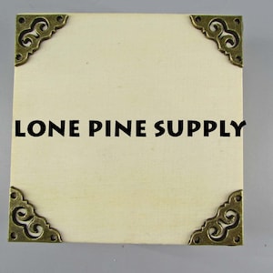 May include: A white square box with four ornate brass corner protectors. The box has the text "LONE PINE SUPPLY" printed in black on the front.