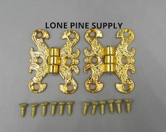 Könnte beinhalten: Zwei goldfarbene Schmetterlings Scharniere mit einem dekorativen Design. Die Scharniere sind mit 12 goldfarbenen Schrauben auf einer grauen Oberfläche befestigt.