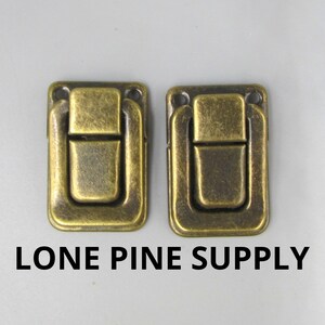 May include: Two antique brass-toned box clasps with a rectangular shape and a simple design. The clasps have a smooth, slightly textured surface.