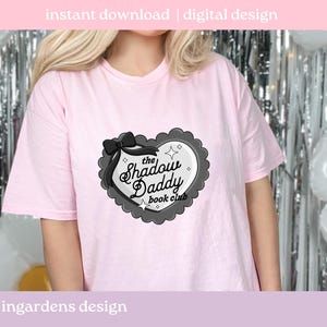 May include: A light pink t-shirt featuring a heart-shaped graphic with the text "the Shadow Daddy book club". The graphic is black and white with a black bow and decorative border. The words "instant download | digital design" are at the top.