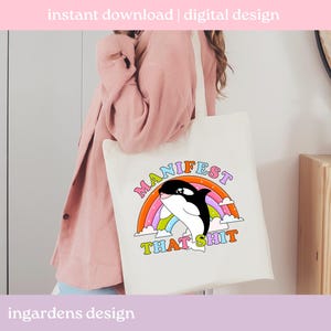 K&ouml;nnte beinhalten: Cremefarbene Tragetasche mit einem Cartoon-Orca-Wal-Design, einem Regenbogen und den Worten "MANIFEST THAT SHIT". Die Tasche hat auch den Text "instant download | digital design" und "ingardens design".