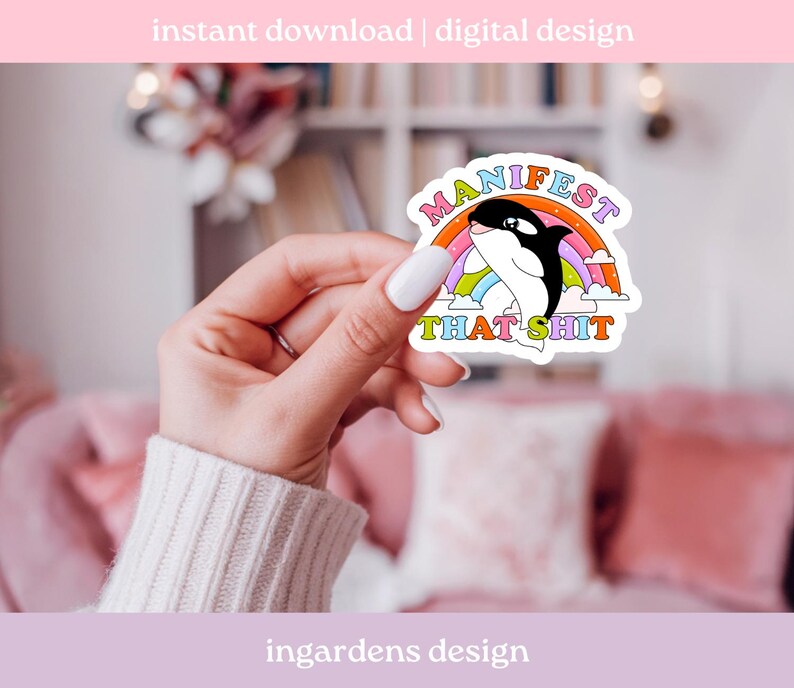 K&ouml;nnte beinhalten: Ein Aufkleber mit einem Cartoon-Orca mit einem Regenbogen und dem Text "MANIFEST THAT SHIT". Der Orca ist schwarz und wei&szlig;, und der Regenbogen hat mehrere Farben. Der Aufkleber wird von einer Hand gehalten.