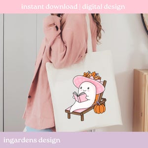 May include: A white tote bag featuring a cartoon ghost wearing a pink hat and reading a book while relaxing on a beach chair. A small orange pumpkin and fall leaves are also depicted. Text at the top reads "instant download | digital design".
