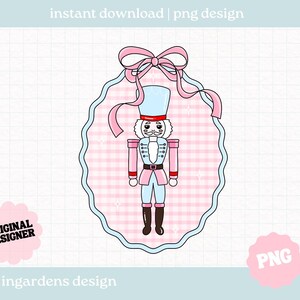 Puede incluir: Un diseño PNG digital con un soldado cascanueces de dibujos animados en rosa y azul. El cascanueces está dentro de un marco ovalado rosa y azul, coronado con un lazo rosa. El texto incluye "instant download | png design", "original designer", y "ingardens design".