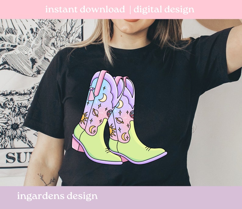 May include: A black t-shirt featuring a graphic of two colourful cowboy boots with a celestial design. The boots are green, pink and blue with stars, moons and planets.