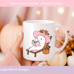 May include: White ceramic mug featuring a cartoon ghost relaxing on a beach chair, wearing a pink hat, and reading a book. A small orange pumpkin sits nearby. The mug has the text "instant download | digital design" and "ingardens design".