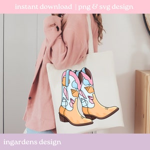 May include: A cream-colored tote bag displays a colorful illustration of cowboy boots. The boots are tan with light blue and pink accents, and feature a seashell design. The text "instant download | png & svg design" is at the top, and "ingardens design" is at the bottom.
