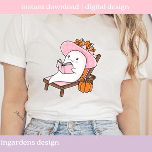 May include: White t-shirt featuring a cartoon ghost wearing a pink hat and reading a book while relaxing on a beach chair. A small orange pumpkin sits nearby. The text "instant download | digital design" is at the top.