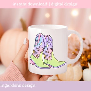 May include: White ceramic mug featuring a colourful illustration of two cowboy boots with a celestial design. The boots are light green, pink and blue with stars, moons and planets.