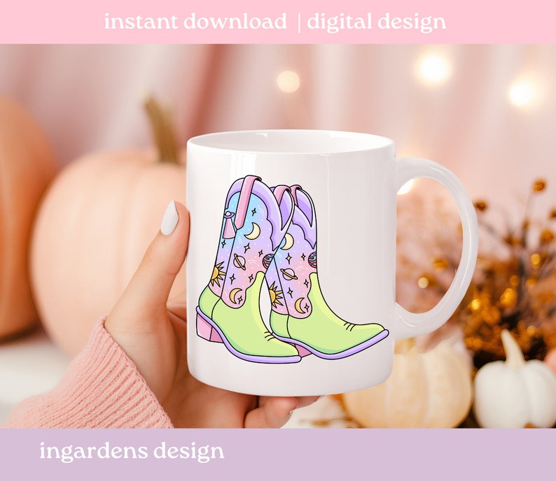 May include: White ceramic mug featuring a colourful illustration of two cowboy boots with a celestial design. The boots are light green, pink and blue with stars, moons and planets.