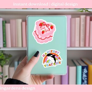 K&ouml;nnte beinhalten: Eine mintgr&uuml;ne Tableth&uuml;lle mit zwei Aufklebern. Einer ist ein rosa Kuchen mit Erdbeeren und dem Text "Just a Girl". Der andere ist ein Aufkleber mit einem Regenbogen, einem Wal und dem Text "Manifest That Shit."