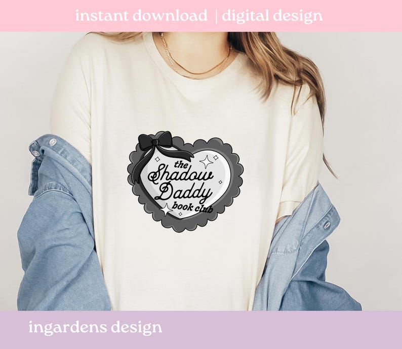 May include: Cream-colored t-shirt featuring a heart-shaped graphic with the text "the Shadow Daddy book club". The graphic is in black and gray with a bow and star accents. The words "instant download | digital design" are at the top.