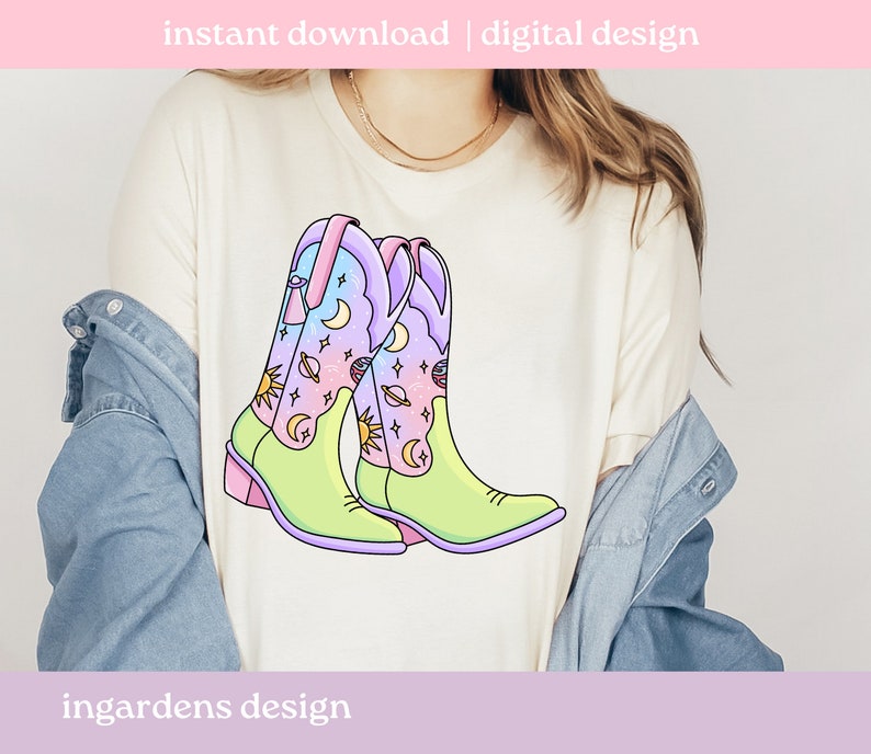 May include: A white t-shirt featuring a graphic of two colourful cowboy boots with a celestial design. The boots are decorated with stars, moons and planets. The text "ingardens design" is at the bottom of the shirt.