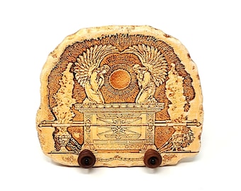 May include: A wooden plaque with a carved image of the Ark of the Covenant, with two angels on either side, and a sun above. The plaque is mounted on a wooden stand.