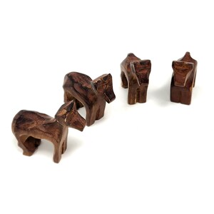 May include: Four small wooden animal figurines, possibly horses, in a brown color. The figurines are standing on a white surface.