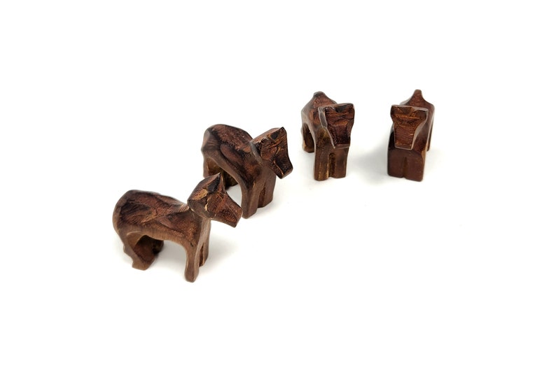 May include: Four small wooden animal figurines, possibly horses, in a brown color. The figurines are standing on a white surface.