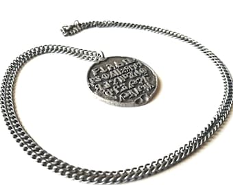 May include: A silver chain necklace with a round pendant featuring an inscription in an old-fashioned font.
