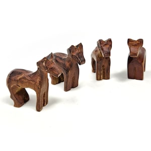 May include: Four wooden animal figurines, possibly horses, standing in a row on a white background. The figurines are all brown and have a simple, carved design.