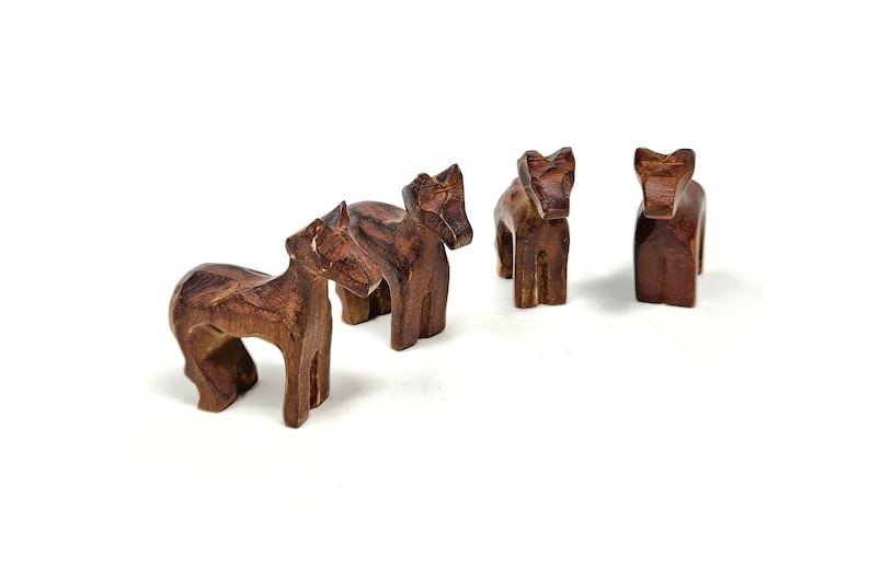 May include: Four wooden animal figurines, possibly horses, standing in a row on a white background. The figurines are all brown and have a simple, carved design.