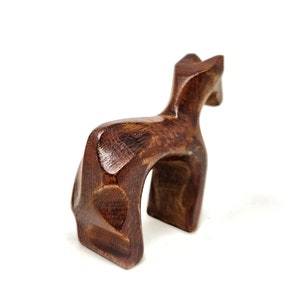 May include: A wooden sculpture of a stylized deer, carved in a dark brown color. The deer is standing on all four legs with its head tilted back.