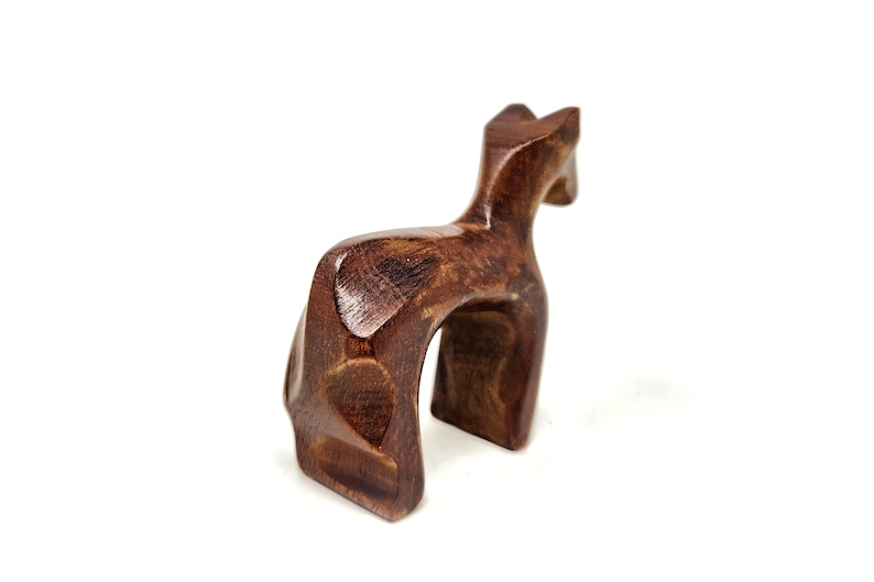 May include: A wooden sculpture of a stylized deer, carved in a dark brown color. The deer is standing on all four legs with its head tilted back.