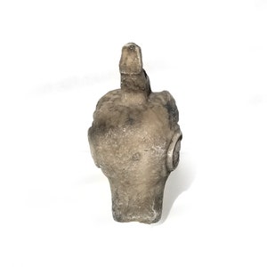 May include: A gray stone sculpture of a bird's head with a long beak. The sculpture is weathered and has a rough texture.