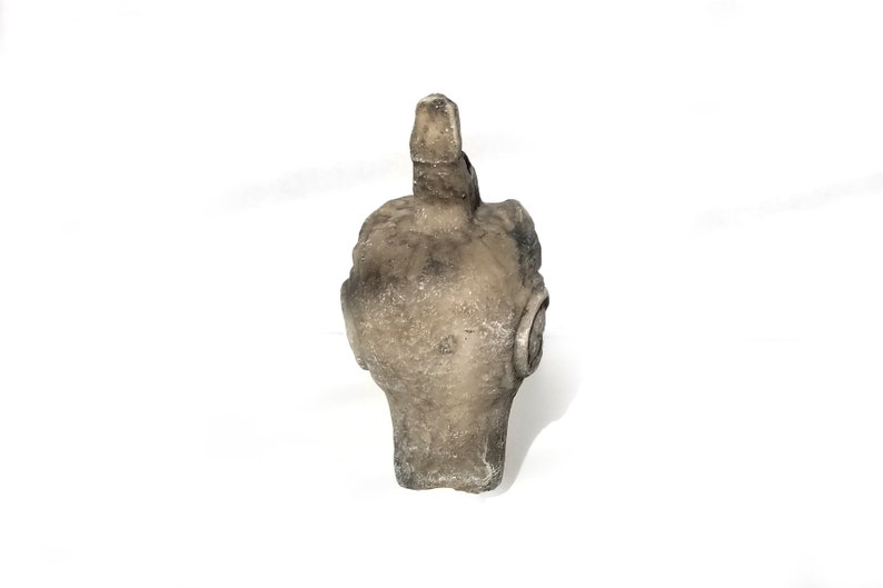 May include: A gray stone sculpture of a bird's head with a long beak. The sculpture is weathered and has a rough texture.