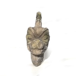 May include: A green and gray stone sculpture of a dragon's head with a fierce expression. The sculpture is carved in detail and has a textured surface.