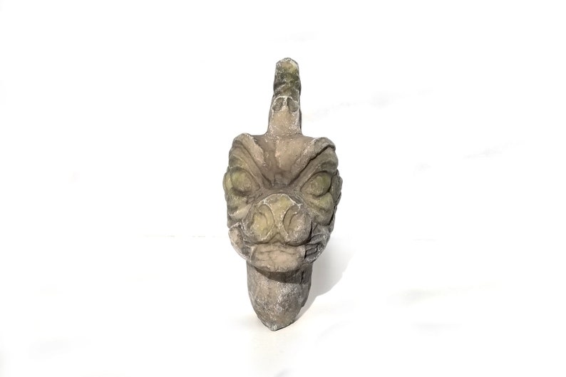 May include: A green and gray stone sculpture of a dragon's head with a fierce expression. The sculpture is carved in detail and has a textured surface.