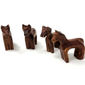 May include: Four wooden horse figurines, each with a unique pose and carved details. The horses are a dark brown color and are arranged in a group on a white background.