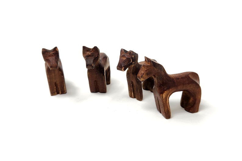 May include: Four wooden horse figurines, each with a unique pose and carved details. The horses are a dark brown color and are arranged in a group on a white background.
