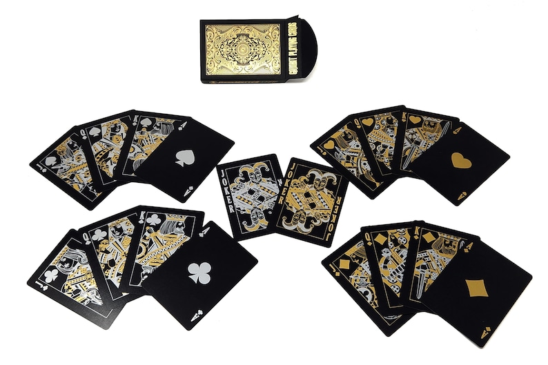 Może przedstawiać: Talia kart do gry z czarnym tłem i złotymi i srebrnymi detalami. Karty są rozłożone wachlarzem, prezentując kolory i figury. Pudełko na karty jest czarne ze złotym filigranem i napisem "COURT PLAYING CARDS".