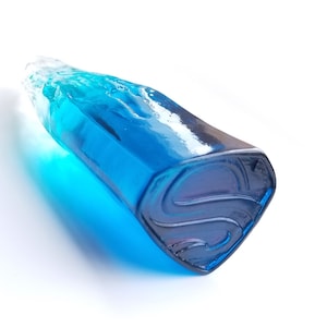 May include: A blue glass sculpture shaped like a Superman logo. The sculpture is translucent and has a light blue colour.