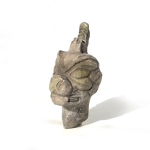 May include: A gray stone sculpture of a dragon head with green eyes. The sculpture is carved in detail and has a weathered look.