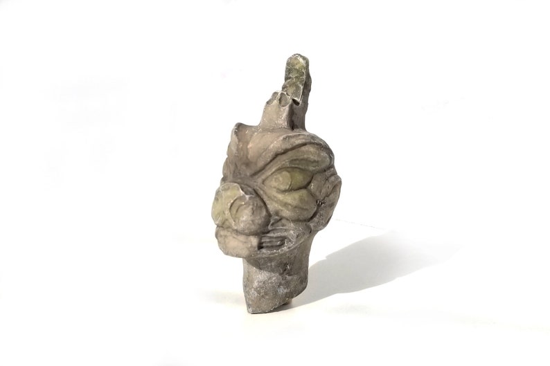 May include: A gray stone sculpture of a dragon head with green eyes. The sculpture is carved in detail and has a weathered look.