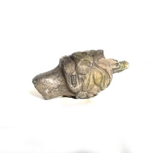 May include: A carved stone sculpture of a face with intricate details. The sculpture is weathered and has a greenish patina.