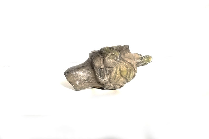 May include: A carved stone sculpture of a face with intricate details. The sculpture is weathered and has a greenish patina.