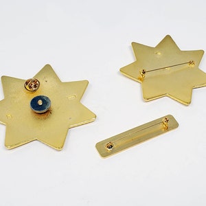 May include: Two gold-toned star-shaped pins with a safety pin closure. The pins are on a white background.