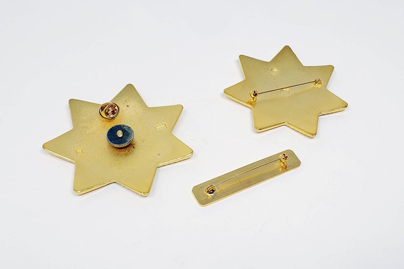 May include: Two gold-toned star-shaped pins with a safety pin closure. The pins are on a white background.
