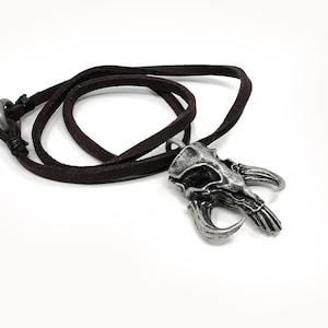 May include: A silver pendant necklace with a detailed skull design and horns. The necklace is on a brown leather cord.
