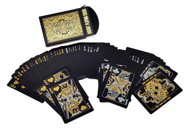Może przedstawiać: Talia czarnych kart do gry ze złotymi detalami, w tym karty z figurami i jokerami. Pudełko na karty, r&oacute;wnież czarne i złote, jest otwarte, a karty są rozłożone wachlarzem. Tekst "EQUIT PLAYING CARDS" jest widoczny na pudełku.