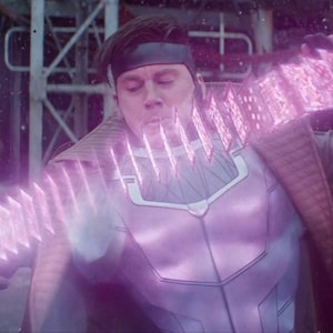 Może przedstawiać: Osoba w fioletowo-białym kostiumie, z czarną opaską na głowie, wydycha energię. Energia przejawia się jako seria świecących, r&oacute;żowych, prostokątnych kształt&oacute;w. Tło to rozmyte otoczenie przemysłowe.