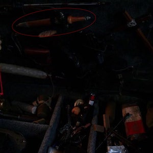 May include: A black and silver knife with a wooden handle is lying on a dark surface. The knife is surrounded by other items, including a metal ring, a wooden stick, and a string of beads.
