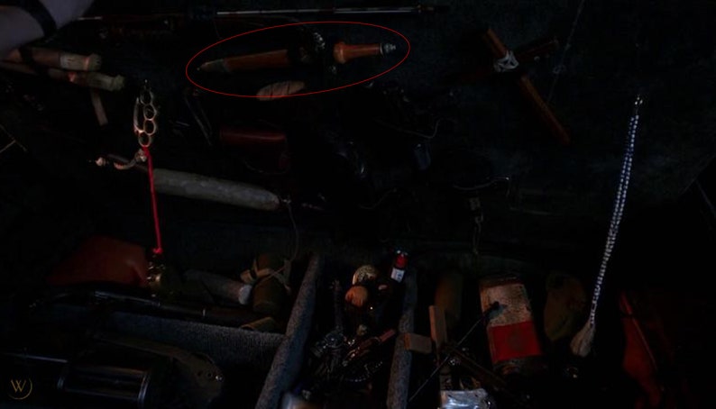 May include: A black and silver knife with a wooden handle is lying on a dark surface. The knife is surrounded by other items, including a metal ring, a wooden stick, and a string of beads.