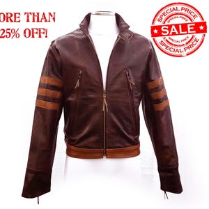 Può includere: Giacca in pelle marrone con strisce beige sulle maniche e chiusura con cerniera. La giacca ha un collo alto e due tasche con cerniera. Il testo "MORE THAN 25% OFF!" e un timbro "SALE" sono visibili.