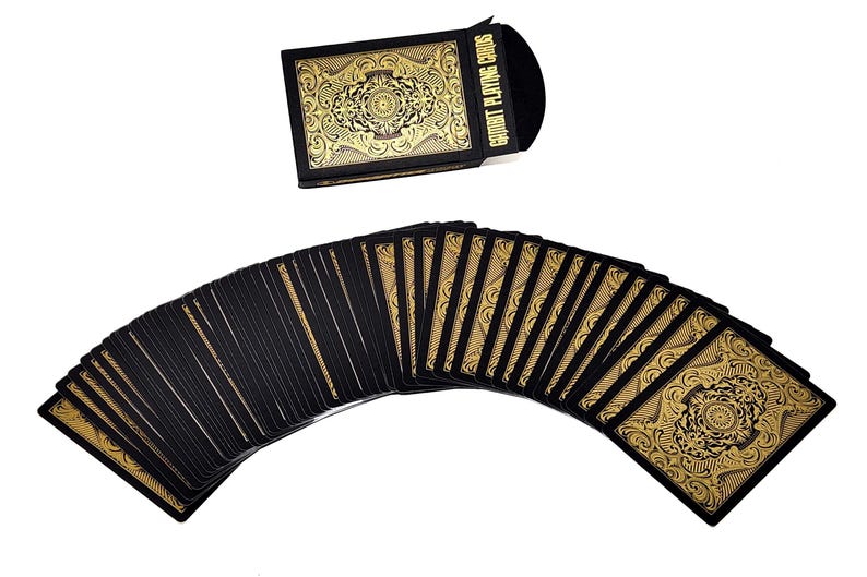 Może przedstawiać: Talia kart do gry z czarnym tłem i złotym wzorem filigranowym. Karty są rozłożone wachlarzem, z widocznym pudełkiem na karty powyżej. Pudełko i rewersy kart mają złoty napis "COURT PLAYING CARDS".