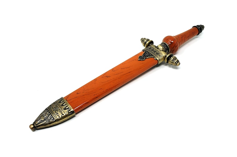 May include: A decorative dagger with an orange wood-like handle and gold-toned metal accents. The handle has a detailed design and the blade is not visible.