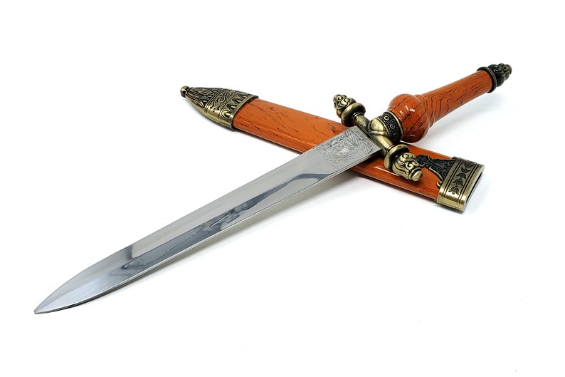 May include: A silver dagger with a brown wooden handle and ornate metal accents. The dagger is in a brown leather sheath with a metal tip.