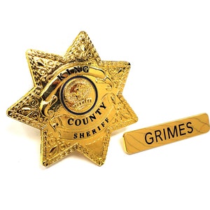 May include: Gold sheriff's star badge with the words "King County Sheriff" and a smaller circle with the word "King" inside. A gold name tag with the word "Grimes" is below the badge.