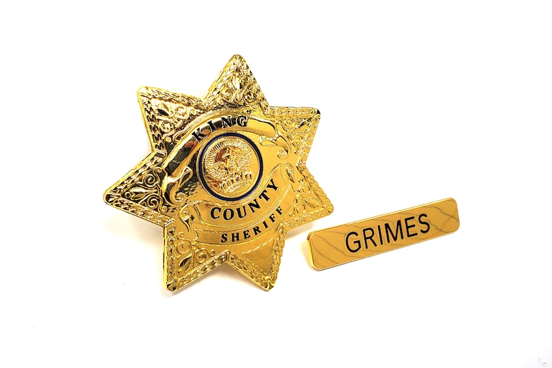 May include: Gold sheriff's star badge with the words "King County Sheriff" and a smaller circle with the word "King" inside. A gold name tag with the word "Grimes" is below the badge.